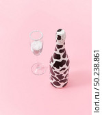 Decorative white painted champagne bottle with black spots and glass of white powder as a snow on a light millennial pink background, copy space. Congratulation card.. Holiday glass of white powder and creative painted wine bottle. Стоковое фото, агентство Ingram Publishing / Фотобанк Лори