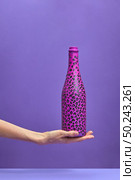 The champagne bottle painted hot pink and black spots on a woman’s hand on a lilac background, copy space. Flat lay. Holiday concept.. Woman’s hand holds painted hot pink and black spots. Стоковое фото, агентство Ingram Publishing / Фотобанк Лори