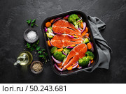 Salmon. Cooking fresh raw salmon fish steaks with vegetables, broccoli, carrot and onion on black background, top view. Стоковое фото, агентство Ingram Publishing / Фотобанк Лори