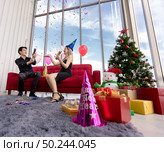 Young asian adult couple celebrating New year and Christmas holiday together with Firecrackers and confetti in living room of big apratment with christmas tree decoration. Стоковое фото, агентство Ingram Publishing / Фотобанк Лори