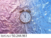 Holiday string of lights and old alarm clock on a duotone pink blue golden background with copy space. Christmas time is at five minutes to midnight.. New Year decor with retro alarmclock and garland. Стоковое фото, агентство Ingram Publishing / Фотобанк Лори