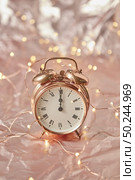 Christmas golden alarm clock on a shiny golden abstract background with copy space. The time is exact midnight. Greeting card.. Holiday card with cooper alarmclock and string of lights. Стоковое фото, агентство Ingram Publishing / Фотобанк Лори