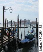 Italian traditional gondola parking near old wooden berth on the background of view of San Giorgio Maggior Church Venice, Italy.. Old wooden pier with parking italian tradition gondola. Стоковое фото, агентство Ingram Publishing / Фотобанк Лори