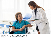 Asian confidence doctor caregiver talking about health concerns with old elderly woman patient sit on wheelchair in hospital ward while daily check up. Стоковое фото, агентство Ingram Publishing / Фотобанк Лори