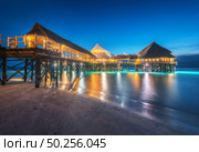 Beautiful wooden restaurant on the water in summer night. Landscape with hotel on the sea, illumination, jetty, sandy beach, blue sky and lights reflected in blurred water at dusk in Zanzibar, Africa. Стоковое фото, агентство Ingram Publishing / Фотобанк Лори