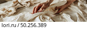 A close-up view captures someones hand as they meticulously sort through a pile of crumpled beige linens. Стоковое AI-изображение, AI-художник Данила Большаков / Фотобанк Лори