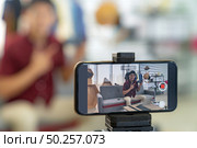 Young asian male online blogger recording live vlog video for review joystick for gaming IT product goods. Online influcencer on social media concept. Focus on mobile phone. Стоковое фото, агентство Ingram Publishing / Фотобанк Лори
