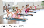 Professional active woman exercising with resistance bands lying on side and stretching legs during group pilates class at gym. Стоковое видео, видеограф Яков Филимонов / Фотобанк Лори