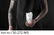 The male barista with tatoo hands makes summer cold fresh beverage in glass from ice cubes, coffee and milk on dark background. 4K UHD video, 240fps, 2160p.. Man barista prepares refreshing drink from ice, coffee and milk with splashes. Стоковое фото, агентство Ingram Publishing / Фотобанк Лори