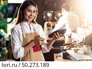 Asian Barista woman make payment with customer credit card using EMV chip technology for coffee purchase at a cafe bar. Cashless preventing from coronavirus covid-19 Spreading and infection. Стоковое фото, агентство Ingram Publishing / Фотобанк Лори