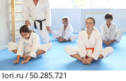Children in white kimono sits in a butterfly pose and practices stretching in sport gym. Стоковое видео, видеограф Яков Филимонов / Фотобанк Лори