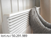Legs in knitted socks warming over electric heater. Frozen woman wearing a warm woolen socks freezing for winter cold. Discomfort spending time at home. Girl warming her feet on modern radiator. Стоковое фото, фотограф Марина Демидюк / Фотобанк Лори