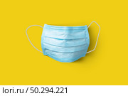 Textile medical antibacterial protective blue face mask on a yellow background, copy space. Concept of prevention from respiratory sickness and viruses.. Medical protective mask on a yellow background. Top view. Стоковое фото, агентство Ingram Publishing / Фотобанк Лори