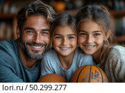 A happy family - a father and two daughters - pose with smiles, hugging and holding basketballs. The atmosphere of warmth, trust and joy emphasizes close family relationships. All three are looking straight into the camera, conveying sincere emotions and positivity. The background is slightly blurred, which emphasizes the faces and facial expressions. Ideal for themes about family values, fatherhood, children's sports and an active lifestyle. Стоковое AI-изображение, AI-художник Анна Кривицкая / Фотобанк Лори