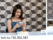 Portrait of asian influencer food blogger or vlog take food photo at new normal social distance restaurant with table shiled partition. Restaurant new normal lifestyle and food influencer concept. Стоковое фото, агентство Ingram Publishing / Фотобанк Лори