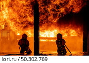 Firefighters using water fog fire extinguisher to fighting with the fire flame in large building. Firefighter and industrial safety disaster and public service concept. Стоковое фото, агентство Ingram Publishing / Фотобанк Лори
