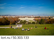 Wonderful landscape with view to Schonbrunn Palace in Vienna, Austria and green wide grass field with sitting and relaxing people on a ground on a blue sky background.. Sitting people on a grass before Schonbrunn Palace in Vienna, Austria. Стоковое фото, агентство Ingram Publishing / Фотобанк Лори