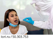 Medical staff with PPE suit test coronavirus covid-19 to asian woman by throat swab at home. New normal healthcare service at home and medical delivery concept. Стоковое фото, агентство Ingram Publishing / Фотобанк Лори