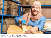 Portrait of Islam Muslim female asian warehouse worker packing and labelling on cardboard box in warehouse environment. Using in business warehouse logistic concept. Стоковое фото, агентство Ingram Publishing / Фотобанк Лори