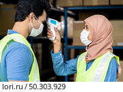 Islam asian warehouse worker take temperature to worker before getting in factory after reopening after city lockdown from COVID-19 coronavirus pandemic in warehouse distribution center environment. Стоковое фото, агентство Ingram Publishing / Фотобанк Лори