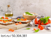 Rye bread bruschetta with cream cheese, olive oil and basil dip, cherry tomatoes, fresh basil leaves on wooden board. Стоковое фото, агентство Ingram Publishing / Фотобанк Лори