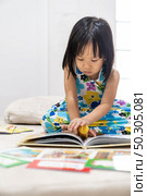 Asian girl child reading interactive book in living room at home as home schooling while city lockdown because of covid-19 pandemic across the world. Home Schooling prepare for Preschool concept. Стоковое фото, агентство Ingram Publishing / Фотобанк Лори