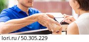 Panoramic Asian woman sign electronic signature to portable mobile device after receive packge from male delivery man in blue shirt. Package shopping delivery and digital sign concept. Стоковое фото, агентство Ingram Publishing / Фотобанк Лори