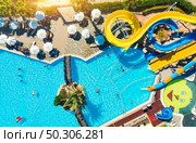 Aerial view of pool, aqua park, swimming people in transparent blue water, umbrellas, sunbeds, green trees at sunset. Summer holidays. Top view of water park. Water slides. Leisure in luxury resort. Стоковое фото, агентство Ingram Publishing / Фотобанк Лори