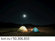 Camping in the mountains under the moon. A tent pitched up and glowing under the sky.. Tourist tents in camp among meadow in the night mountains. Стоковое фото, агентство Ingram Publishing / Фотобанк Лори