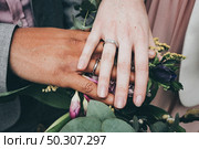 A selective closeup shot of a Caucasian female and African American male wearing rings and holding flowersDiversity concept. a Caucasian female and African American male wearing rings and holding flowersDiversity concept. Стоковое фото, агентство Ingram Publishing / Фотобанк Лори