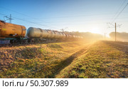 Moving freight train in fog at sunrise in autumn. Industrial landscape with train in motion, railroad, green grass, trees, gold sunbeams, foggy trees, blue sky in fall. Railway station. Transportation. Moving freight train in fog at sunrise in autumn. Industrial. Стоковое фото, агентство Ingram Publishing / Фотобанк Лори
