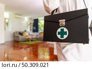 Close up medical staff in personal protective equipment PPE suit with background of asian woman with face mask waiting in living room of apartment .Delivery coronavirus covid-19 test at home concept. Стоковое фото, агентство Ingram Publishing / Фотобанк Лори
