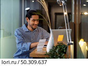 Young adult Asian businessman sitting at coffee bar in office with laptop. Smart office work everywhere concept. Стоковое фото, агентство Ingram Publishing / Фотобанк Лори