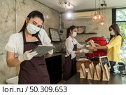 Asian waitress take order from mobile phone for takeout and curbside pickup orders while city lockdown. They wear protective face mask to prevent from infection of coronavirus COVID-19 pandemic. Стоковое фото, агентство Ingram Publishing / Фотобанк Лори
