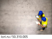 Top view of two industrial workers wearing hardhats and reflective jackets holding tablet and checklist on gray concrete background.. Top view of two industrial workers wearing hardhats and reflective jackets. Стоковое фото, агентство Ingram Publishing / Фотобанк Лори