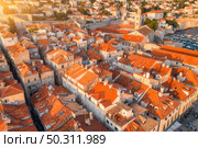 Aerial view of houses with orange roofs at sunset in summer in Dubrovnik, Croatia. Top view of beautiful architecture in old city. Historical centre, buildings, walking people on the street. Travel. Стоковое фото, агентство Ingram Publishing / Фотобанк Лори