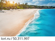 Aerial view of white sandy beach, ocean with waves, umbrellas, green palms at sunset. Summer holiday in Zanzibar, Africa. Tropical landscape with palm trees, sand, blue water, people, sky. Top view. Стоковое фото, агентство Ingram Publishing / Фотобанк Лори