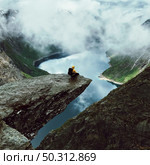 Man sits at the end of Trolltunga before the mountains. Стоковое фото, агентство Ingram Publishing / Фотобанк Лори