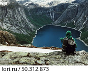 Man sits at the end of Trolltunga before the mountains. Стоковое фото, агентство Ingram Publishing / Фотобанк Лори