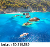 Speed boat on blue sea at sunrise in summer. Aerial view of motorboat on sea bay, rocks in clear azure water. Tropical landscape with yacht, stones, mountain, green trees. Top view. Oludeniz, Turkey. Стоковое фото, агентство Ingram Publishing / Фотобанк Лори