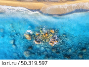 Aerial view of clear blue sea with waves, stones and rocks, empty sandy beach at sunset. Summer in Oludeniz, Turkey. Tropical seascape with azure water. Top view of sea coast. Nature background. Стоковое фото, агентство Ingram Publishing / Фотобанк Лори