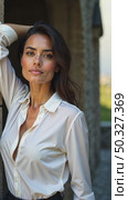 A caucasian young woman in a white blouse standing confidently with her arm scratches and ruffles her hair against a textured stone wall, soft lighting enhancing. Стоковое AI-видео, аниматор Sergey Grishin / Фотобанк Лори
