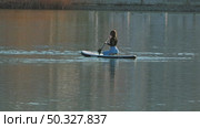 A woman kneeling on a paddleboard and gently paddling into the calm waters of a lake. Dressed in a black top and light blue jeans. Riding a sup board. Russia, January 30, 2025. Редакционное видео, видеограф Воловодов Владимир / Фотобанк Лори