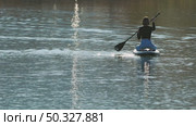 A young woman gracefully paddles across a calm body of water sitting on a sup board, her figure reflected in the shimmering surface. The sunlight dances on the water, creating a serene atmosphere. Стоковое видео, видеограф Воловодов Владимир / Фотобанк Лори