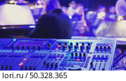A vibrant music scene, focusing on a sound mixing console in the foreground, with blurred musicians in the background illuminated by blue lights, creating an energetic atmosphere. Стоковое видео, видеограф Воловодов Владимир / Фотобанк Лори
