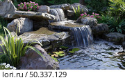 A garden featuring a waterfall cascading into a pond, creating a serene and beautiful landscape. Стоковое AI-изображение, AI-художник Данила Большаков / Фотобанк Лори