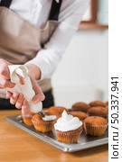 young woman decorating cupcakes with white whipped cream by squeezing confectionery bag. Стоковое фото, агентство Ingram Publishing / Фотобанк Лори