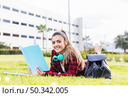 portrait smiling female university student lying green grass holding book hand. Стоковое фото, агентство Ingram Publishing / Фотобанк Лори