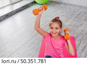 portrait smiling girl exercising with orange dumbbell. Стоковое фото, агентство Ingram Publishing / Фотобанк Лори