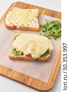High angle of wooden board with parchment paper and toasted bread slices with cheese and vegetables and sauce before combining into delicious sandwich.. Preparation of tasty sandwich with cheese. Стоковое фото, агентство Ingram Publishing / Фотобанк Лори
